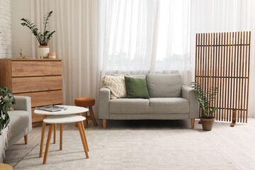 Interior of living room with comfortable sofa, chest of drawers, coffee table and folding screen