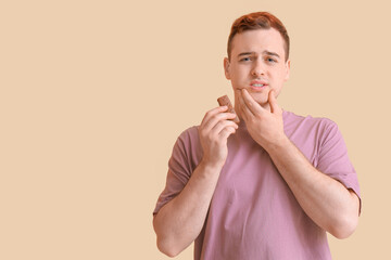 Young man with chocolate suffering from tooth ache on beige background