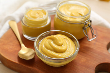 Board with bowl and jars of mustard on wooden background