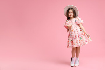Stylish little girl wearing oversized high heeled shoes on pink background, space for text