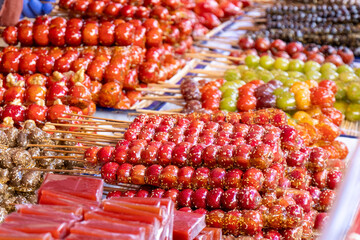 Many colorful tanghulu, a traditional Chinese snack. They are made with various fruits such as strawberries, grapes, and hawthorns, coated in a hard candy shell.
