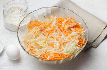 Chopped cabbage and grated carrots in glass bowl with ingredients for healthy homemade cooking
