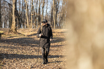 A man walking along a leafy path in a tranquil forest, enjoying the beauty of nature while using trekking poles for support.