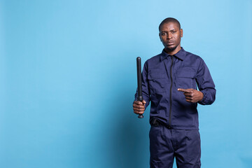 Trained security guard pointing at his baton against blue background, showing his police weapon in...