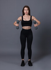 Woman in sportswear exercising with dumbbells on grey background