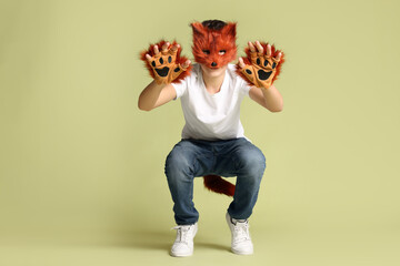 Quadrobics. Boy wearing fox mask, gloves and tail on pale olive background