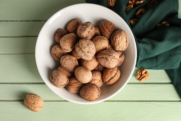Bowl with tasty walnuts on green wooden background