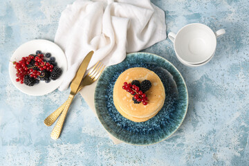 Plate of sweet pancakes with fresh blackberries and red currants on light blue background