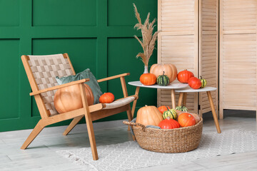 Armchair with folding scree, coffee table and wicker basket of different pumpkins near green wall
