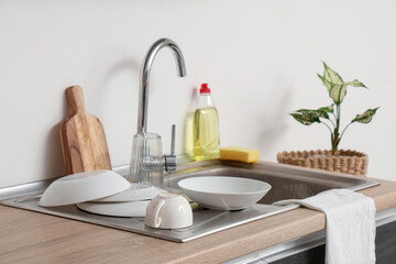 Clean dishes, napkin, detergent and houseplant near sink in light kitchen