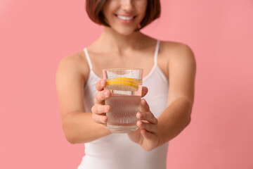 Young woman with glass of infused water on pink background