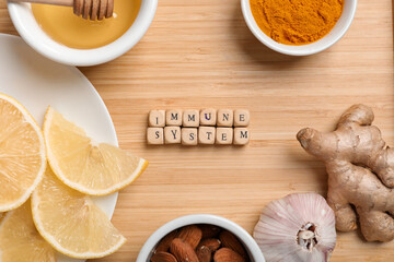 Text IMMUNE SYSTEM, lemon, honey, turmeric powder, ginger and garlic on wooden background, closeup