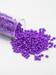 Purple masterbatch granules spilling from glass tube on white background, polymer carrier of color pigment in plastic industry. Perfect for plastic company catalog design