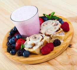 Fluffy cinnamon swirls served on wooden board with milk smoothie and fresh berries ..