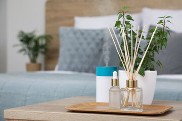 Aroma reed diffuser with essential oil on tray and houseplant on table in room. Closeup