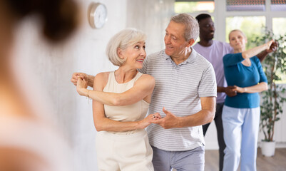 Cheerful senior woman practicing passionate samba with interested man in dance class for adults....