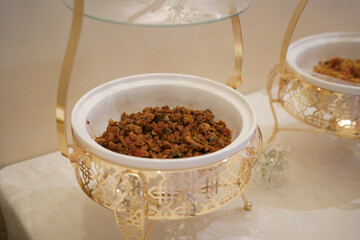 A beautifully presented Middle Eastern dish served in an elegant golden chafing dish, typically enjoyed during Ramadan or festive gatherings in Saudi Arabia. The traditional meal is rich in spices and