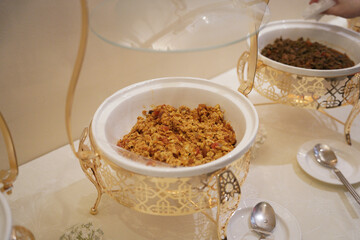 A beautifully presented traditional Saudi Arabian dish served in an ornate golden chafing dish, typically enjoyed during Ramadan or festive gatherings. The meal, rich in flavors and spices, is an esse