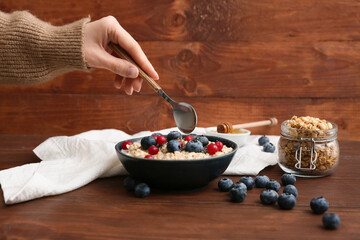 Female hand with tasty oatmeal and berries on wooden background