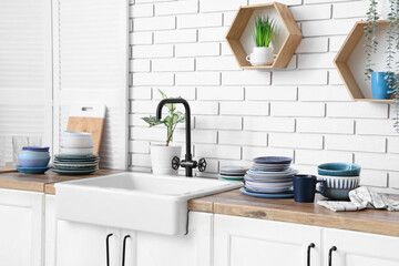 Different plates and sink on wooden table near white brick wall in kitchen