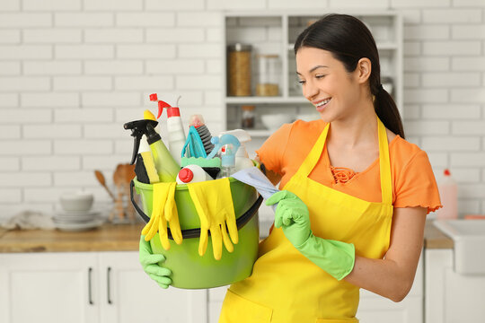 Young woman with bucket full of cleaning supplies in kitchen