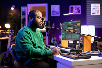 Composer thinking about new rhymes to fit into the new song, writing down verses to produce a track in his home studio. Professional artist songwriter making music for his debut album.