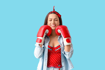 Young pin-up woman in boxing gloves on blue background. Women's History Month