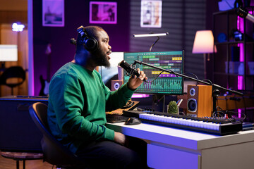 Artist composer recording a new track on his home studio microphone, editing his song with professional gear. Adjusting volume levels and adding sound effects, mix and master.