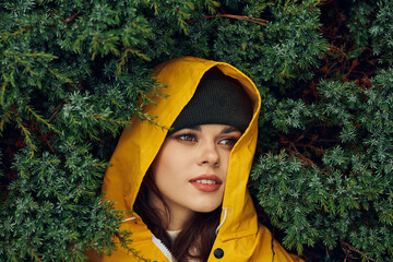A young woman in a yellow raincoat hiding behind evergreen trees during a rainy day adventure in...
