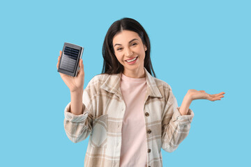 Beautiful young woman with modern power bank on blue background