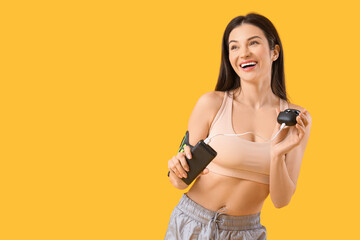 Sporty young woman with modern power bank charging wireless earbuds on yellow background
