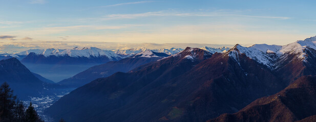 Snowy village is nestled in mountain valley at dusk, surrounded by towering peaks and mist, creating peaceful and remote alpine scene, Piani di Bobbio, Italy