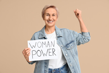 Beautiful mature happy woman holding paper with text WOMAN POWER on beige background. Women history...