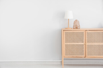 Lamp with statuette on stylish wooden chest of drawers near white wall in room