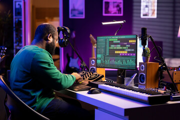Skilled male composer producing new songs on his mixing console, operating on professional gear in home studio. Artist audio engineer twisting knobs to adjust sound levels on tracks.