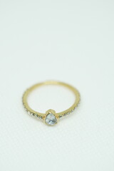 Close-up of a delicate gold ring with a teardrop-shaped clear gemstone and side stones, placed on a...