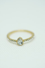 Close-up of a delicate gold ring with a teardrop-shaped clear gemstone and side stones, placed on a...