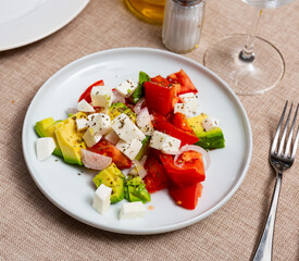 Fresh salad made of avocado, tomato, cheese and onion rings served in a plate on the table