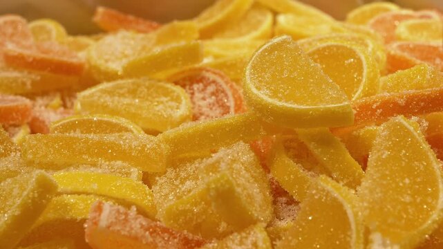 A colorful mix of yellow and orange jelly candies shaped like citrus slices, coated in sugar. This close-up shot captures the texture and sweetness, ideal for food, dessert, or market-related projects