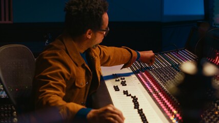 African american sound producer connecting coiled cable on mixing console, processing and editing...