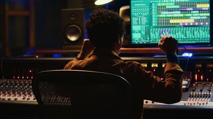 African american sound engineer feeling happy with his recorded song on mixing console, working in...