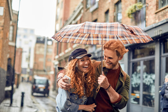 Young couple taking a selfie while under an umbrella avoiding rain
