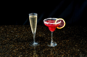 Margarita made of blood orange and a tall glass of champagne on a black background