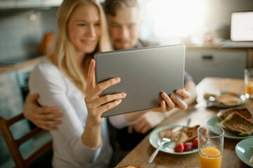 Young couple using a digital tablet while having breakfast in the morning