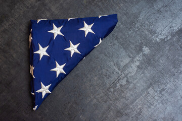 Folded American flag resting on a dark background, symbolizing patriotism and tribute.