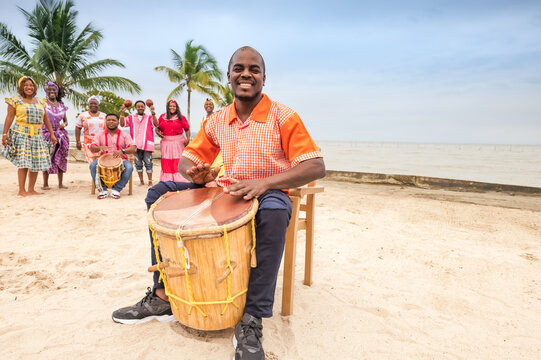 Young Latino man of the Garifuna ethnic group plays the drum with joy, his friends dance in the background.
