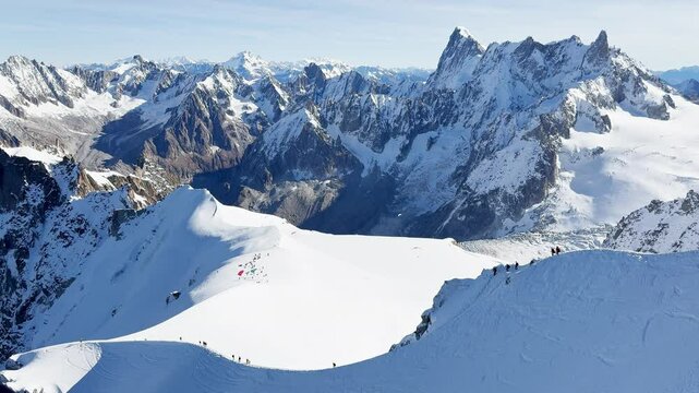 Paragliders with backpacks descend the steep snowy slopes of Aiguille du Midi, Chamonix, preparing for a parachute jump between the majestic peaks of the French Alps, with aamazing view of Mont Blanc