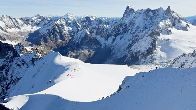 Paragliders with backpacks descend the steep snowy slopes of Aiguille du Midi, Chamonix, preparing for a parachute jump between the majestic peaks of the French Alps, with amazing view of Mont Blanc