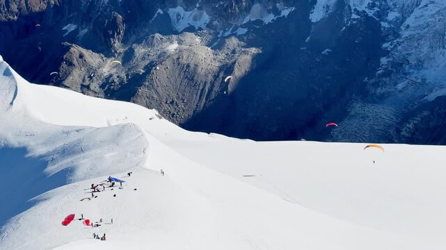Paragliders with backpacks descend the steep snowy slopes of Aiguille du Midi, Chamonix, preparing for a parachute jump between the majestic peaks of the French Alps, with amazing view of Mont Blanc