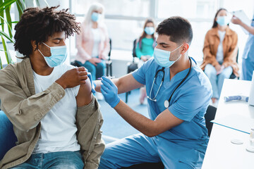 Doctor holding syringe making vaccination injection dose in shoulder of African American guy...